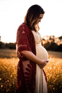 Pregnant woman standing in a field touching her belly